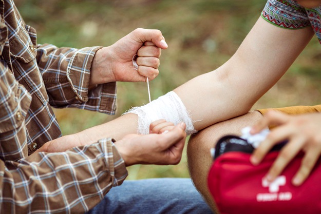 person wrapping his friends injured arm | Camping Checklist For The Wild Man